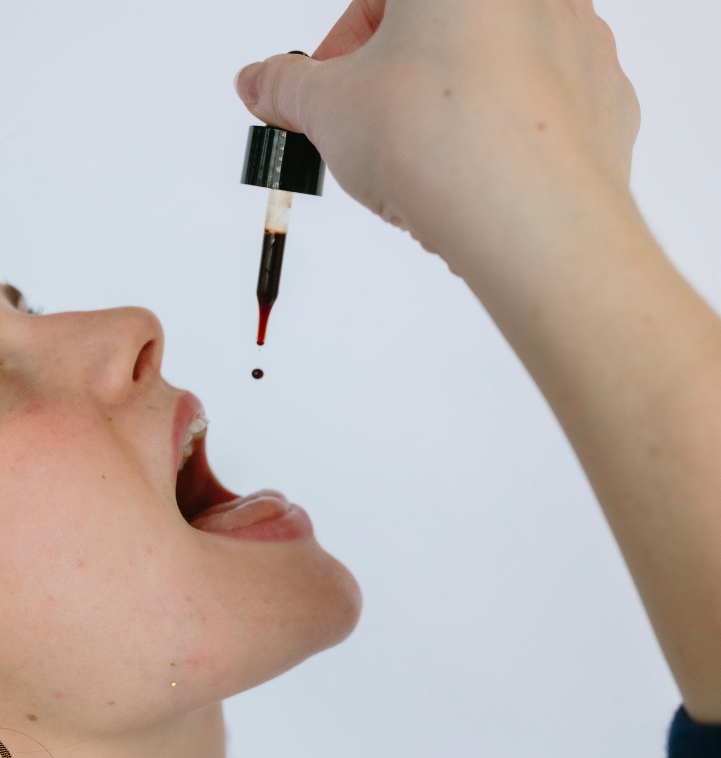 Person dropping a liquid from a dropper into their mouth against a white background