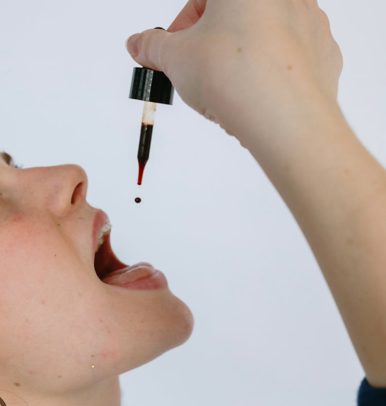 Person dropping a liquid from a dropper into their mouth against a white background